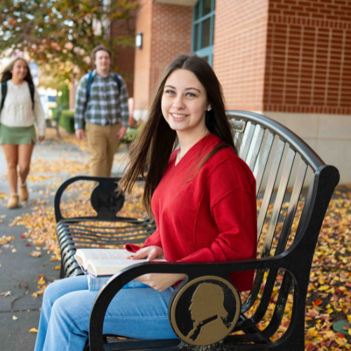 A student sitting on a bench outside of campus in the fall.