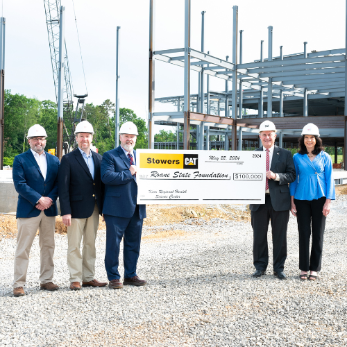 Five people standing at a construction site holding a large check.