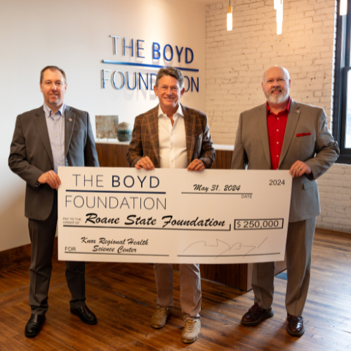 Three men hold a large check in an office.