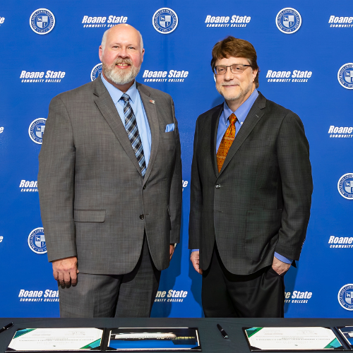 Two people standing in front of a Roane State background.